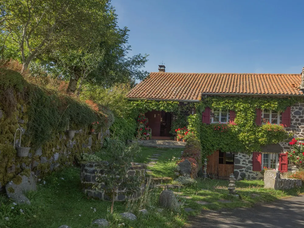 Maison de pierre couverte de lierre, volets rouges et toit de tuiles
